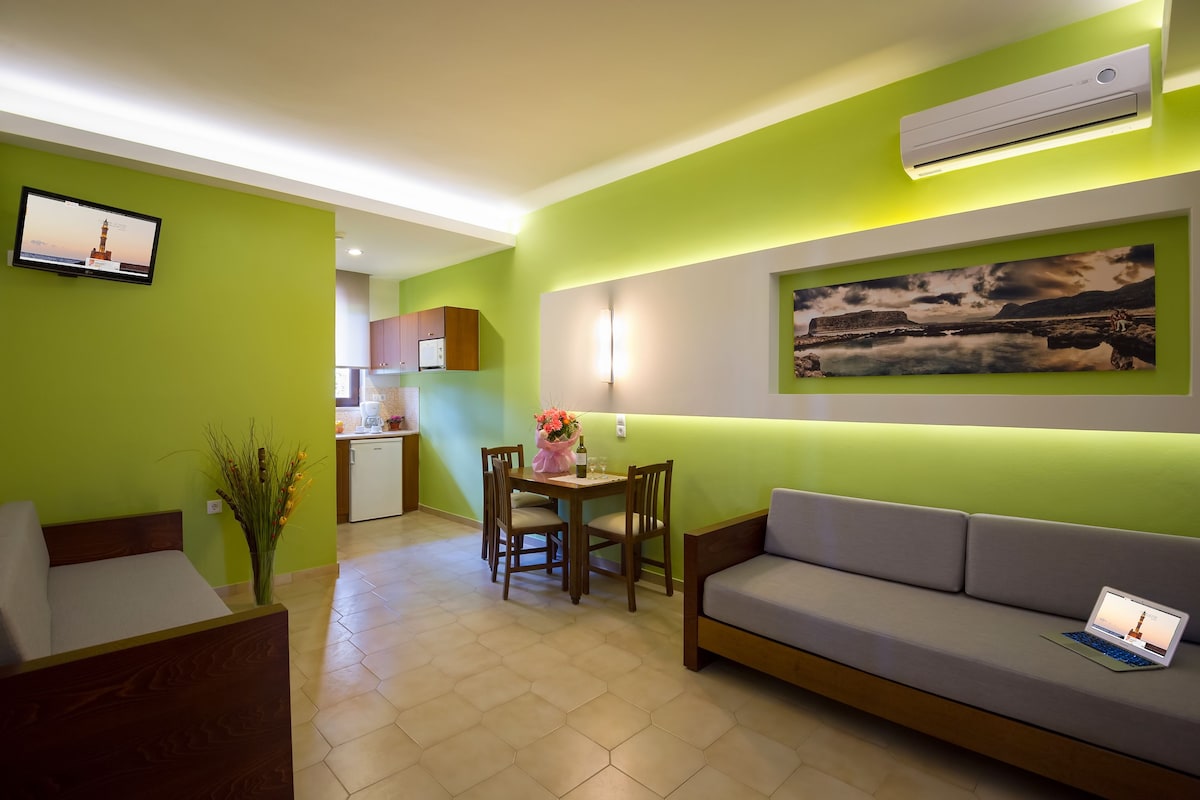A modern living room with a sofa, a dining table with chairs, a TV mounted on the wall, and a painting above the sofa.