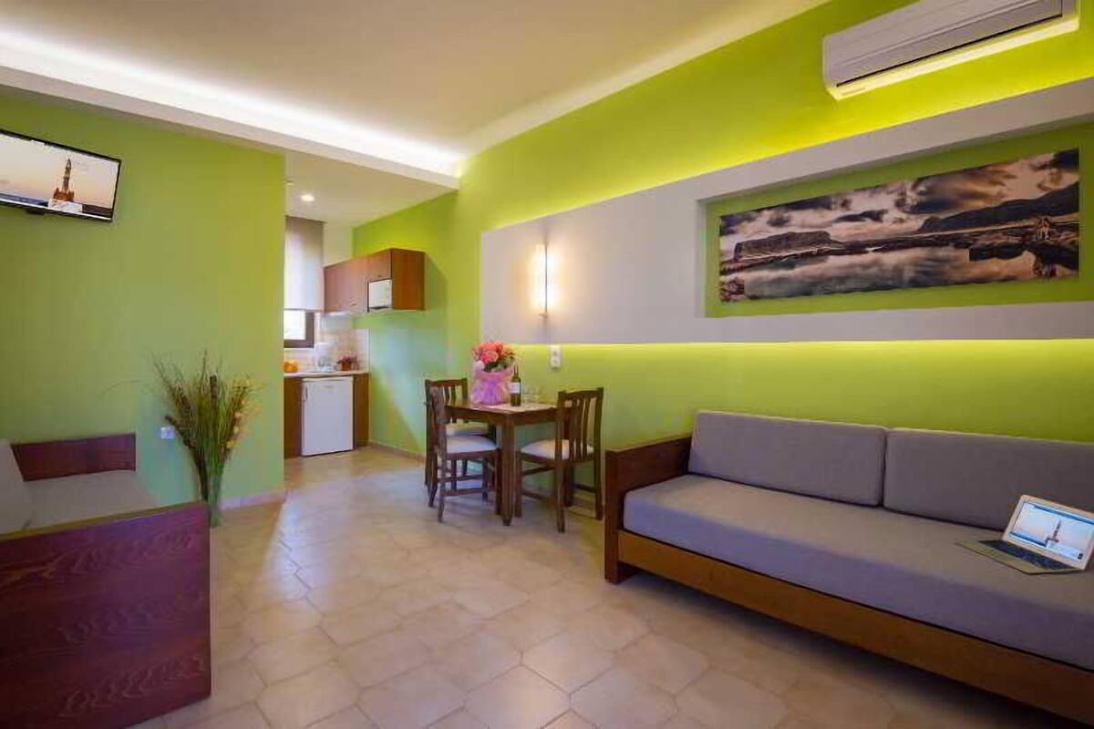 A modern living room with a sofa, a dining table with chairs, and a TV mounted on the wall.