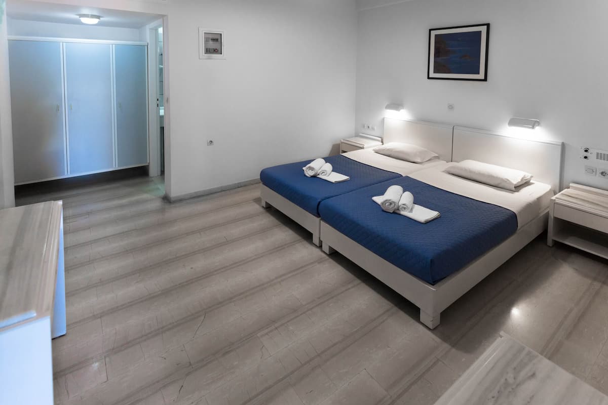 A modern hotel room with two beds, a wardrobe, a nightstand, and a wall-mounted lamp.
