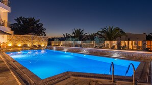 A swimming pool with a stone wall and palm trees in the background. - Anna Maria Village (Hersonissos)
