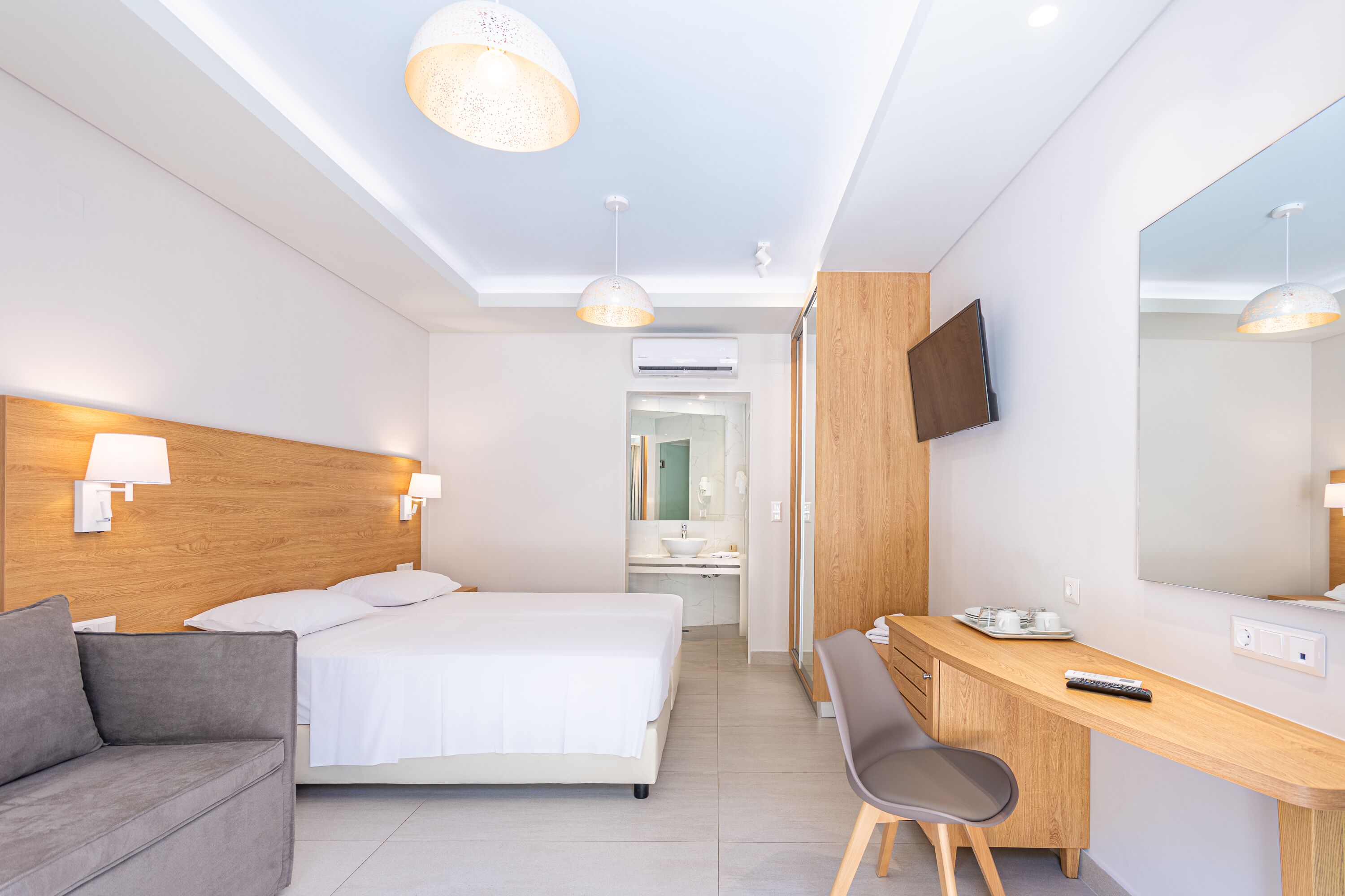 A modern hotel room with a bed, a desk, a chair, a TV, and a large mirror.