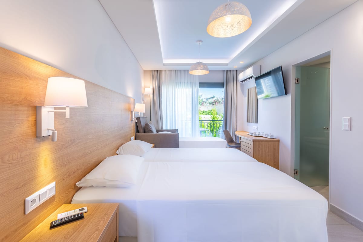 A hotel room with a large bed, bedside tables, a TV, and a balcony with curtains.