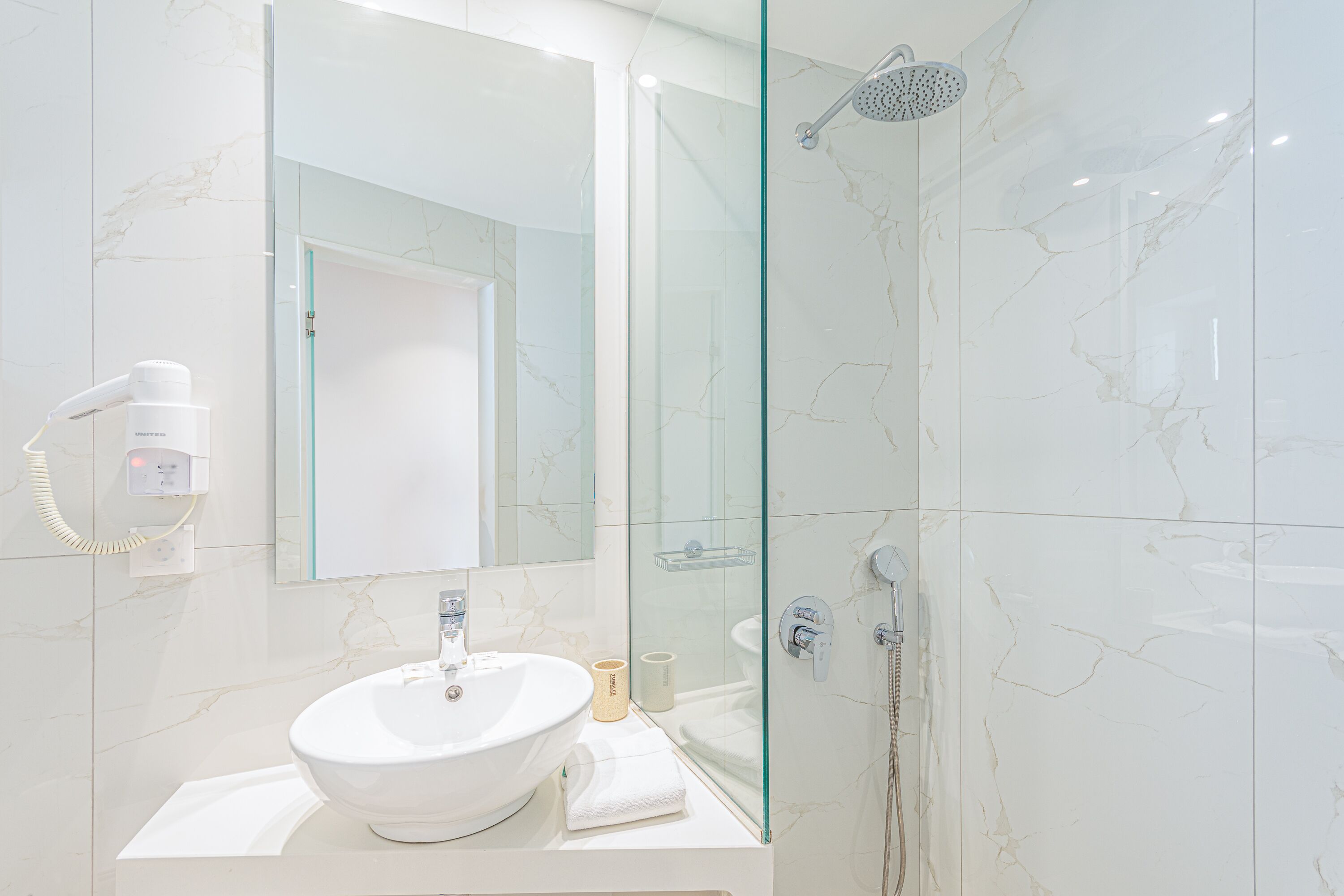Un baño moderno con lavamanos blanco, espejo y cabina de ducha con mampara de vidrio.