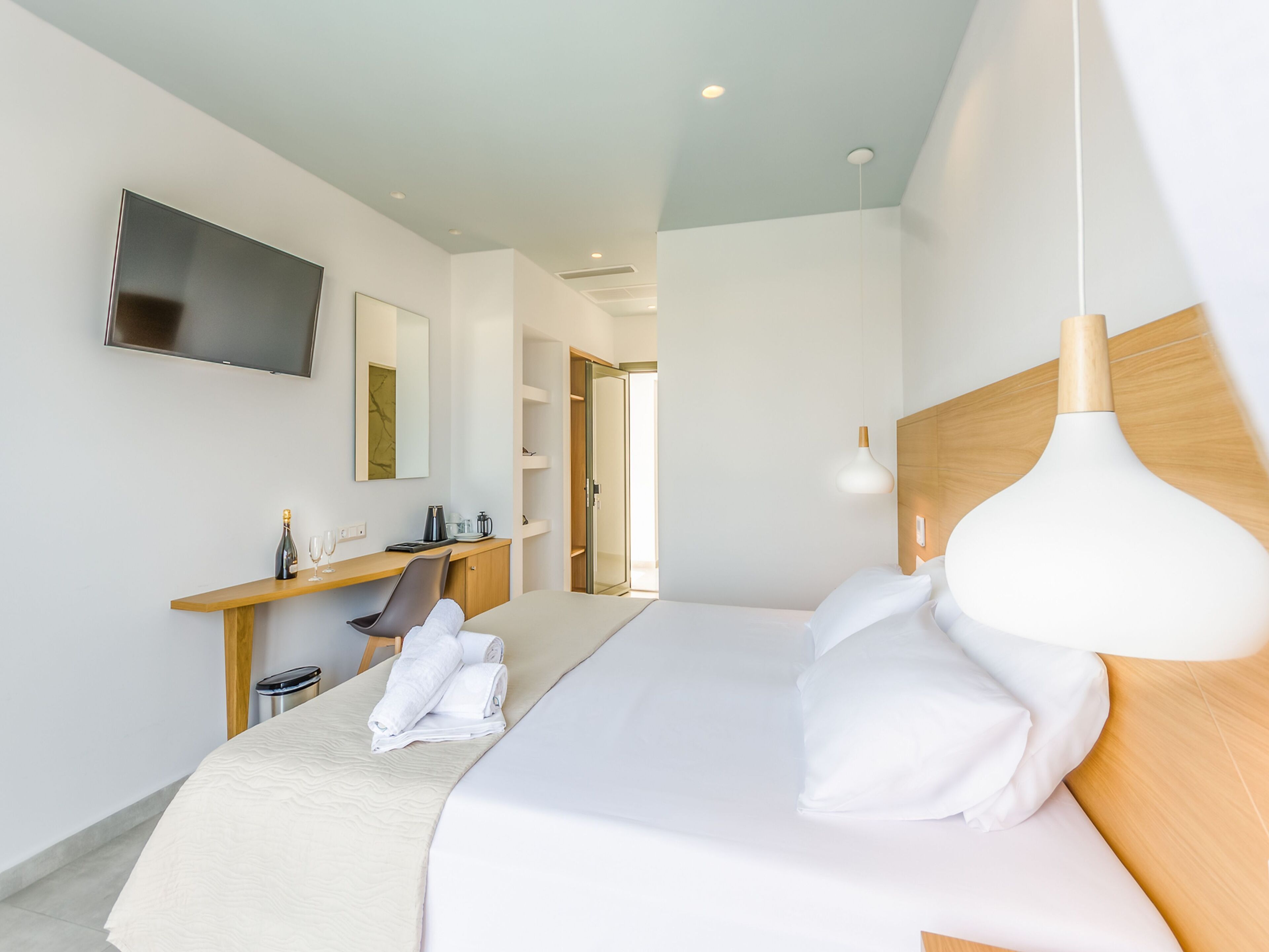 Una habitación de hotel moderna con una cama grande, un escritorio con silla, un televisor montado en la pared y una lámpara colgante.