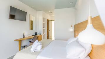 Una habitación de hotel moderna con una cama grande, un escritorio con silla, un televisor montado en la pared y una lámpara colgante.