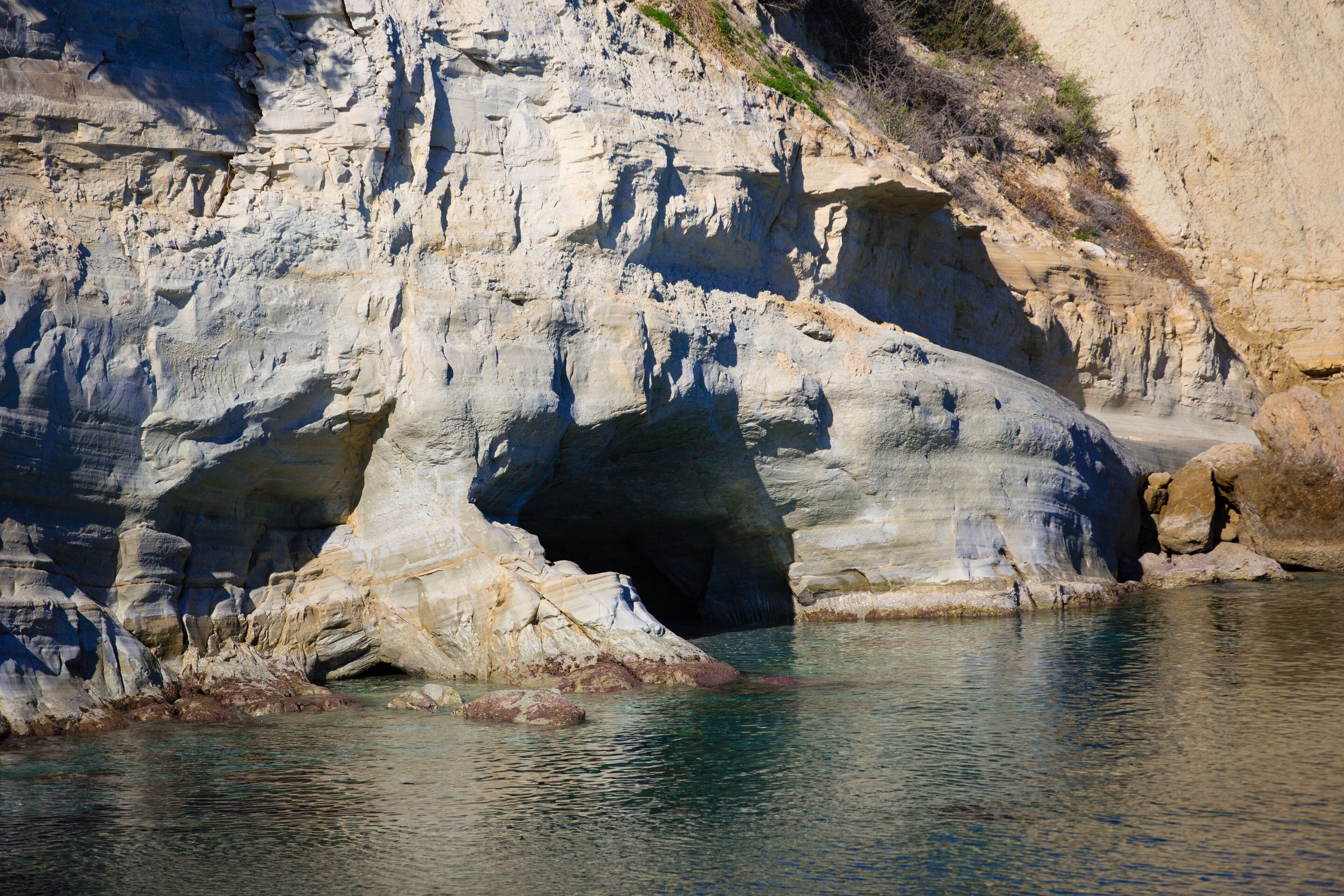 A natural rock formation with a cave entrance and clear water.