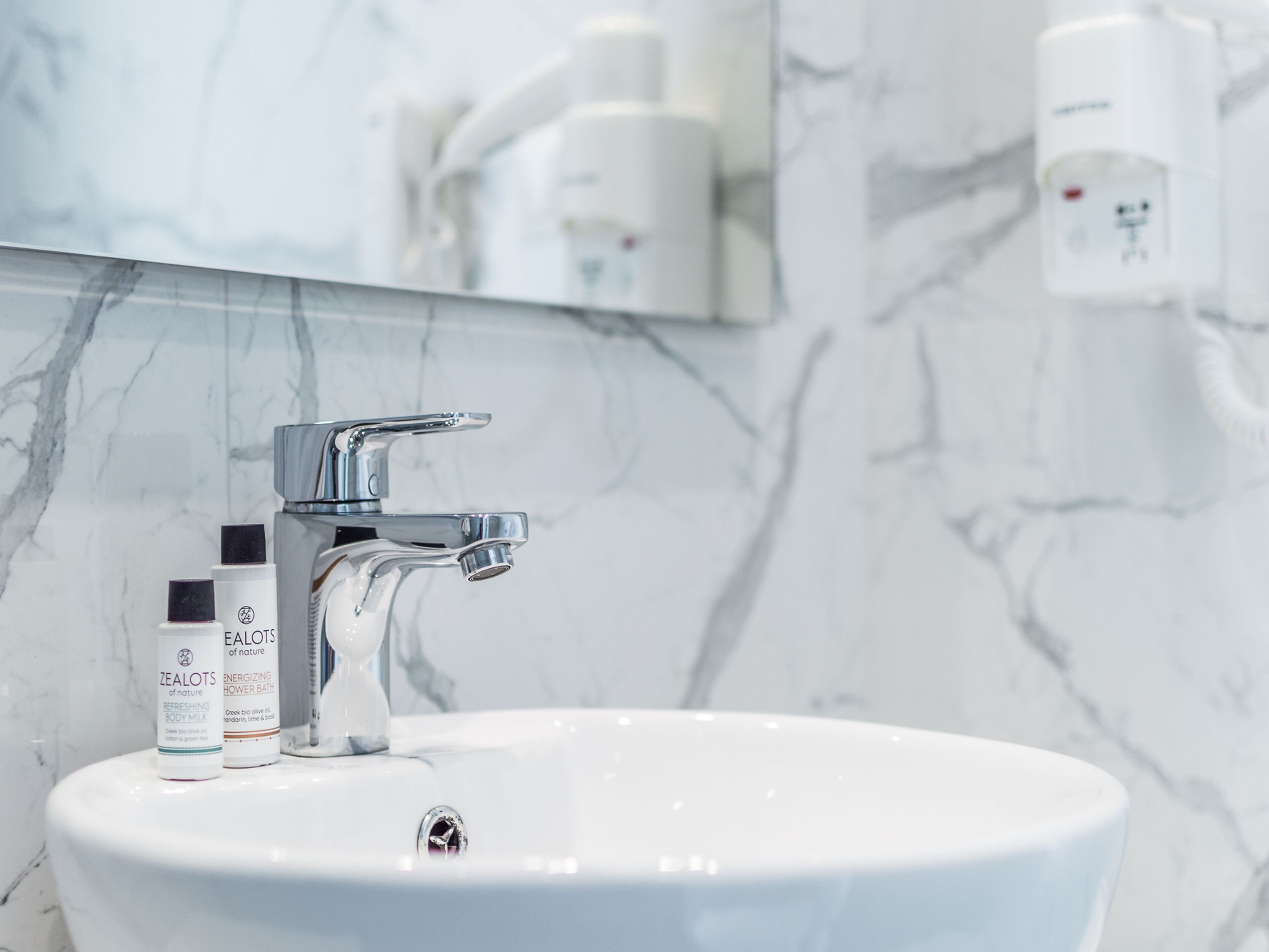 A bathroom with a white sink, chrome faucet, and two bottles of Zealots body milk.