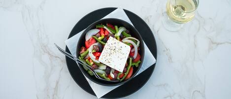 A salad on a black plate with a white napkin, a fork, and a glass of white wine on a marble surface.