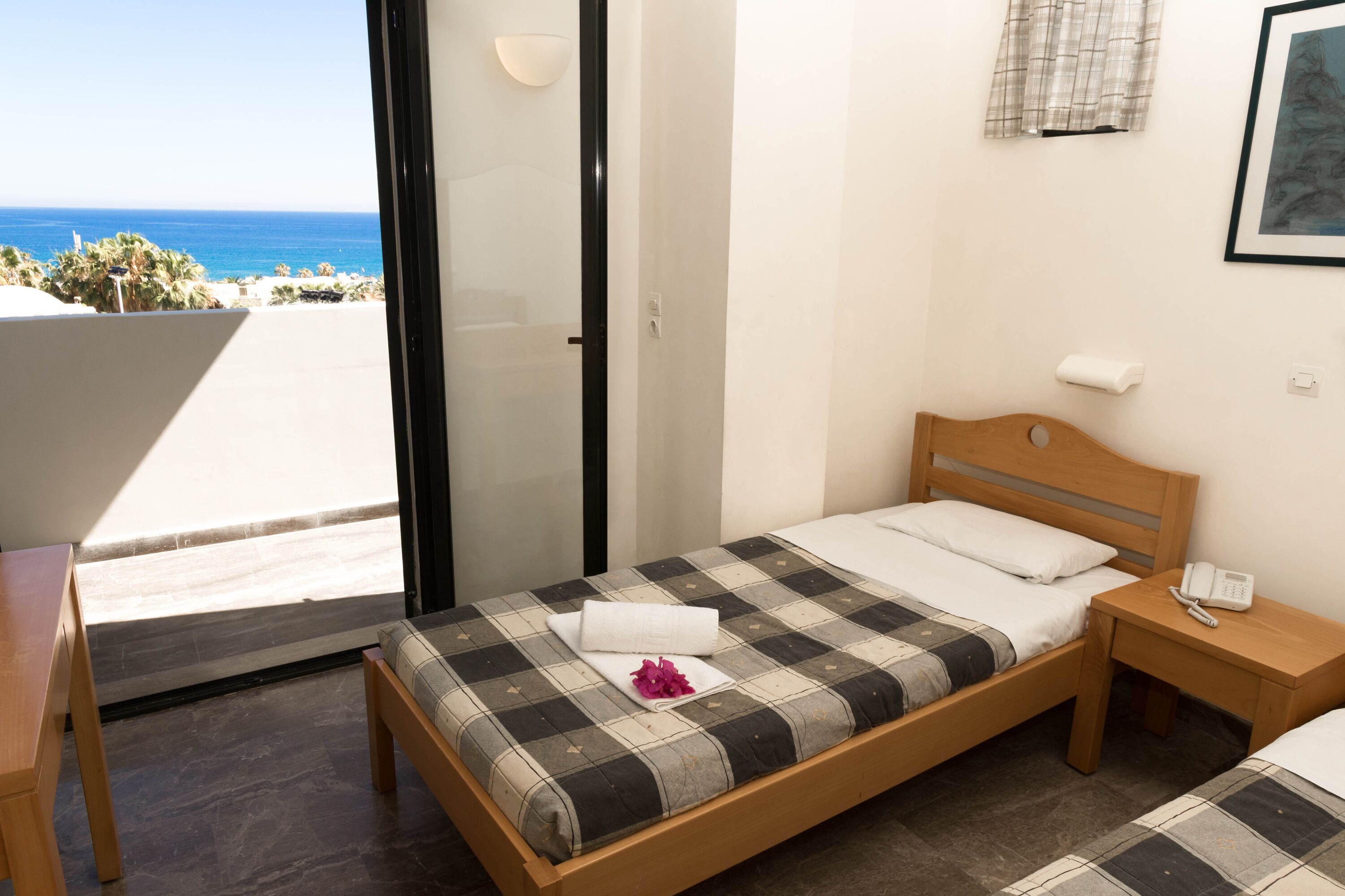Un dormitorio con cama, mesita de noche, ventana con vista al océano y una puerta.
