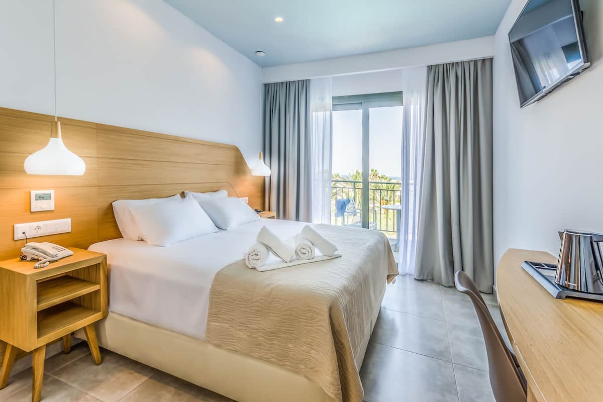 A hotel room with a bed, bedside table, lamp, TV, and a balcony with curtains.