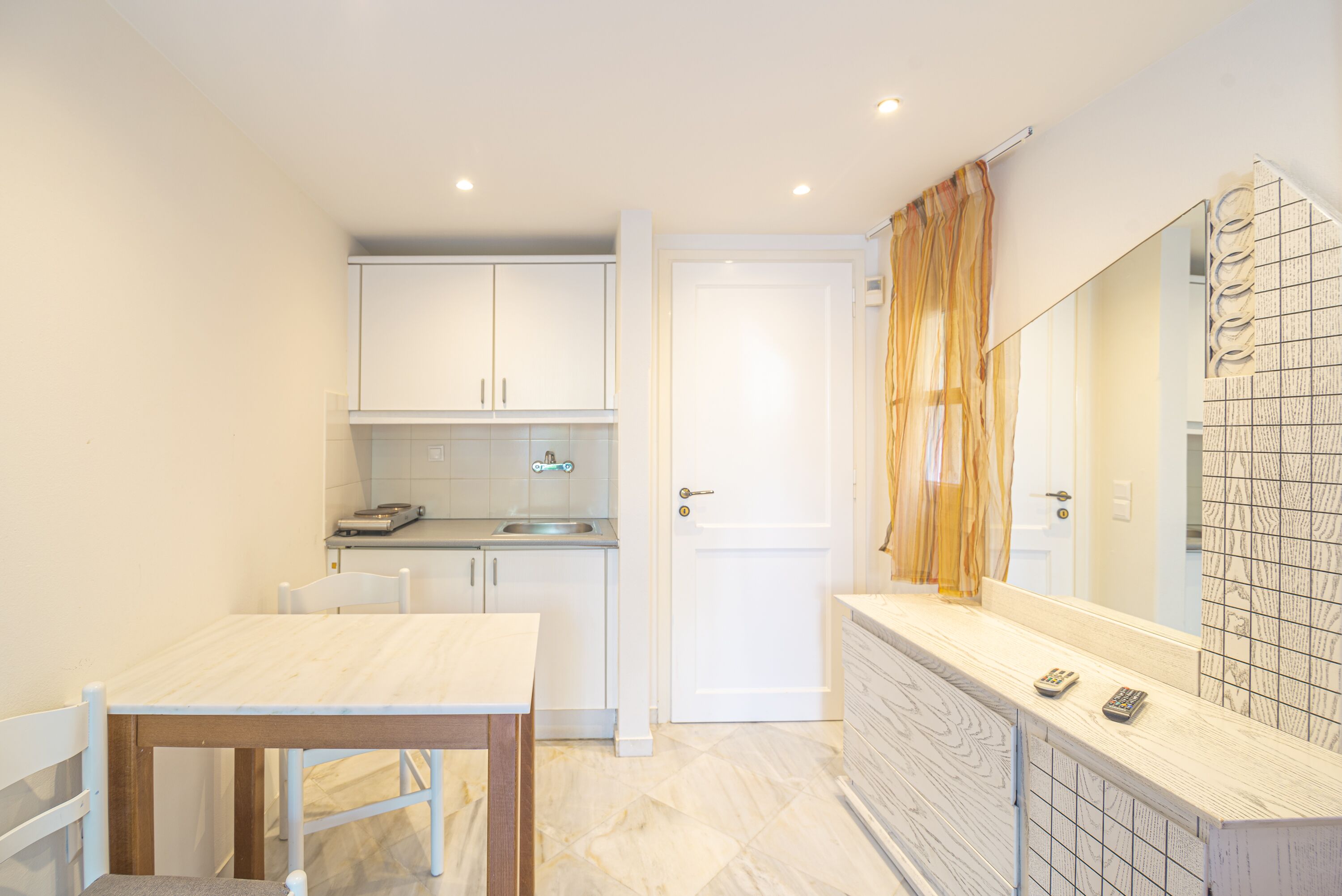 Una cocina compacta con armarios blancos, una mesa de madera y un salpicadero azulejado.