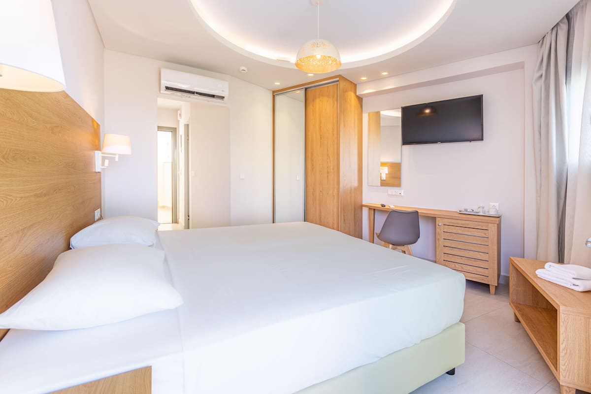 A modern hotel room with a large bed, a desk, a chair, a TV, and a wardrobe.