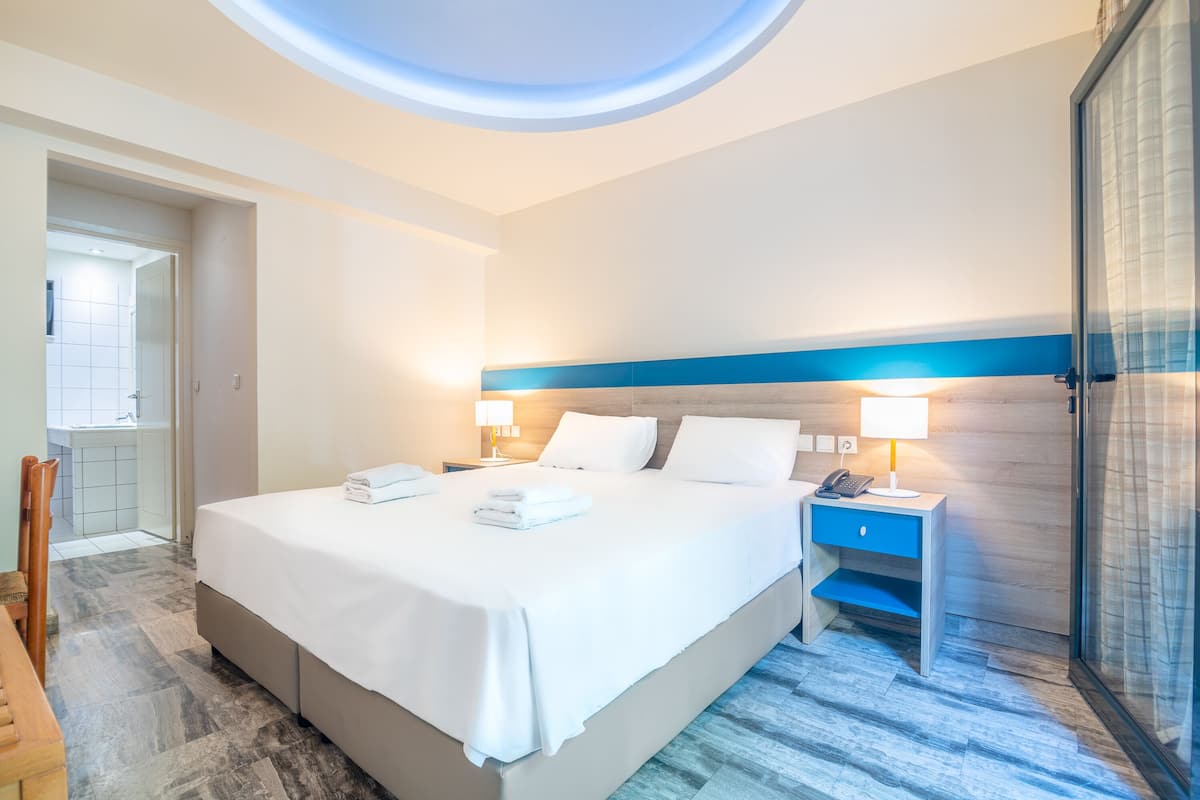 A hotel room with a large bed, bedside tables, a desk, and a view of the sky through a skylight.