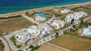 Vista aérea de un complejo turístico costero con edificios blancos, piscina y playa.
