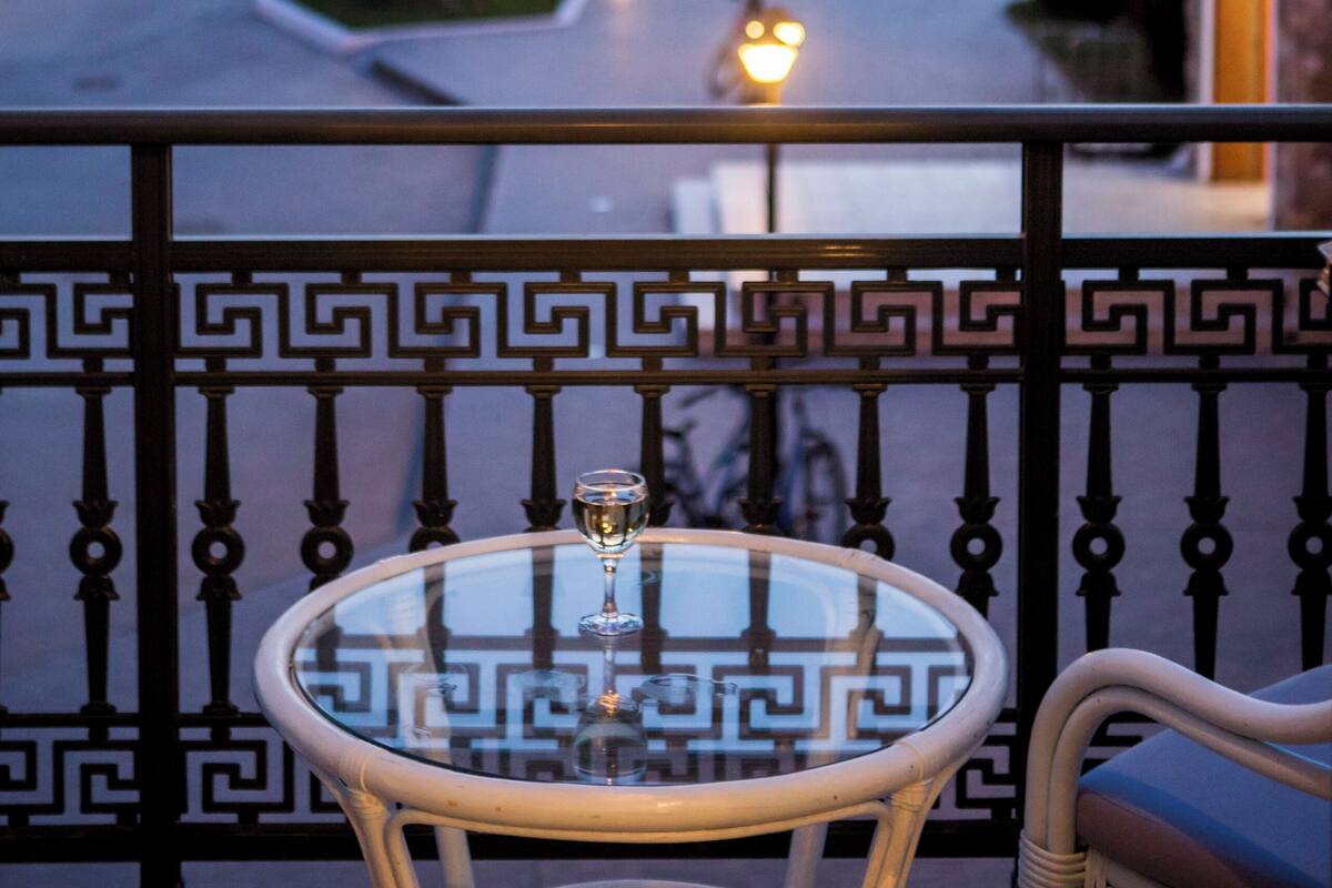 A balcony with a glass table, a chair, and a view of a street at dusk.