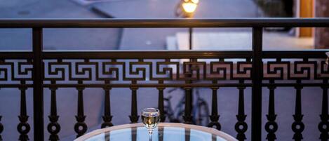 A balcony with a glass table, a chair, and a view of a street at dusk.