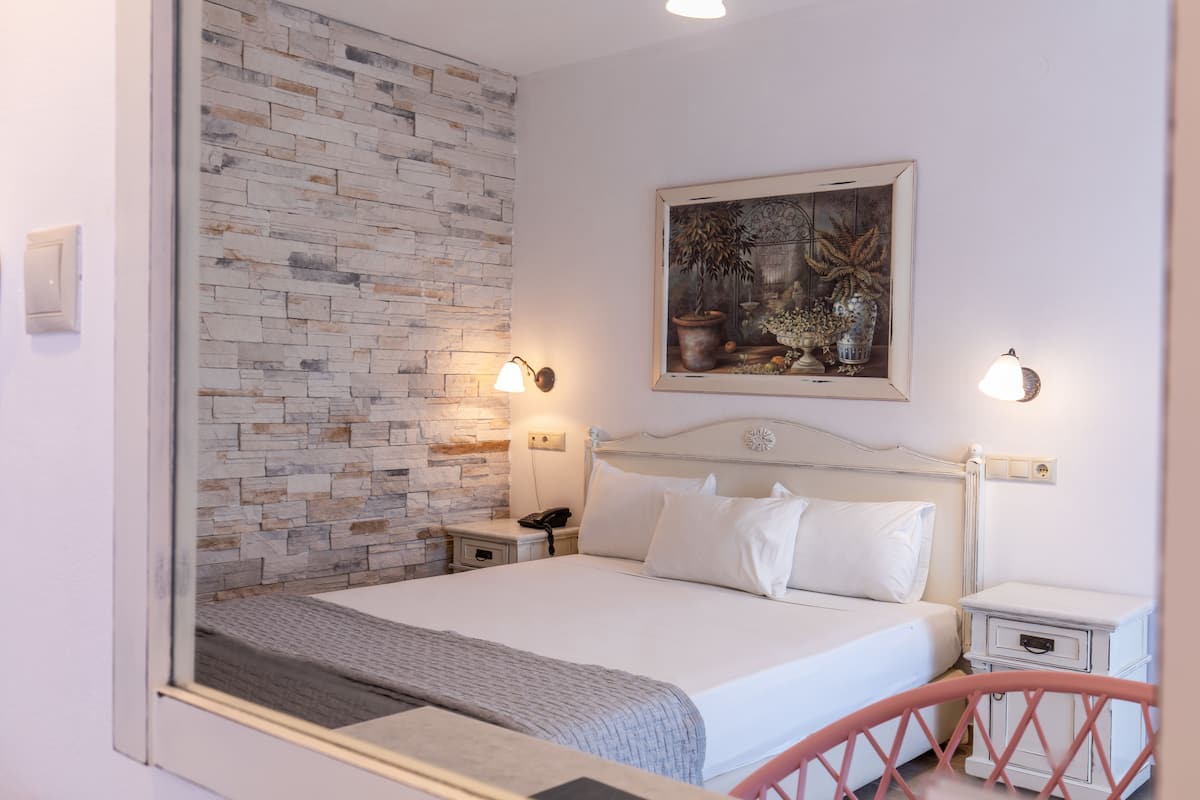 A hotel room with a brick accent wall, a bed with white linens, two bedside tables with lamps, and a framed artwork above the bed.