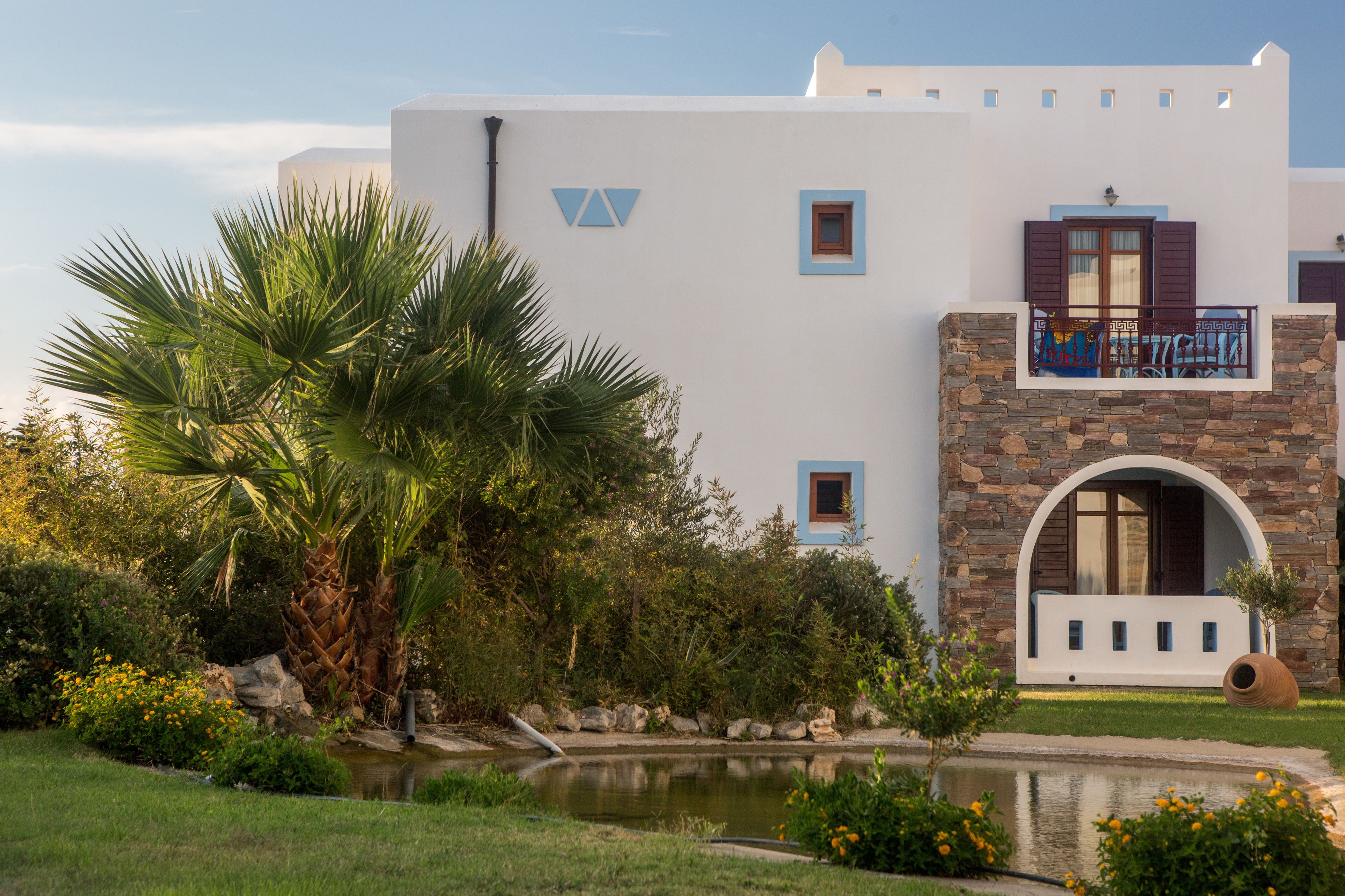 A modern building with a white facade, a stone archway, and a small balcony with a view of the surrounding greenery.