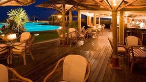Un área de bar al aire libre con mobiliario de mimbre y una piscina al fondo.