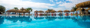 A pool with clear blue water, surrounded by red lounge chairs and thatched umbrellas. - Plaza Beach Hotel (Naxos)
