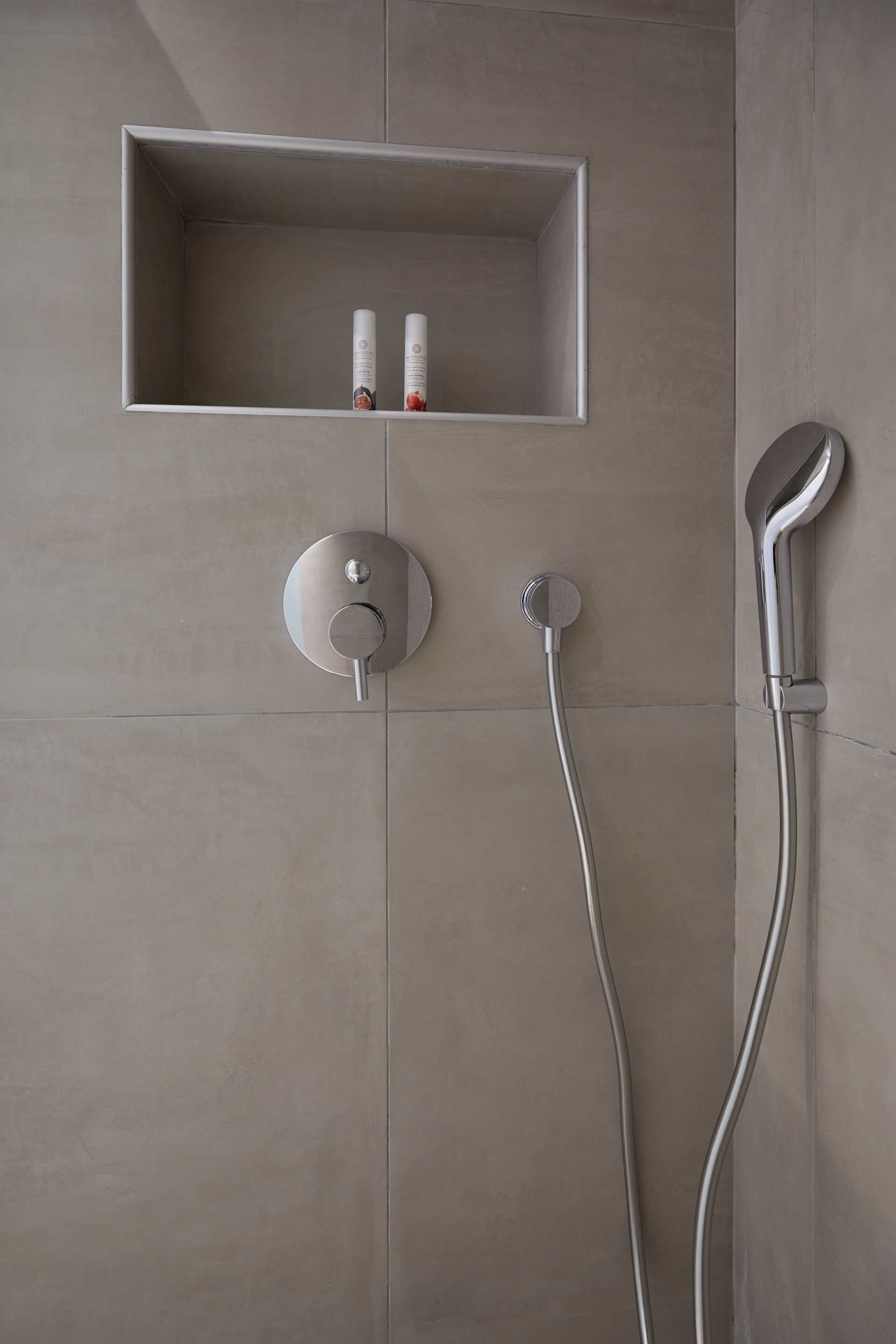 Un espace douche moderne doté d’un panneau de commande mural, d’un pommeau de douche à main et d’une étagère contenant des flacons de produits de toilette.