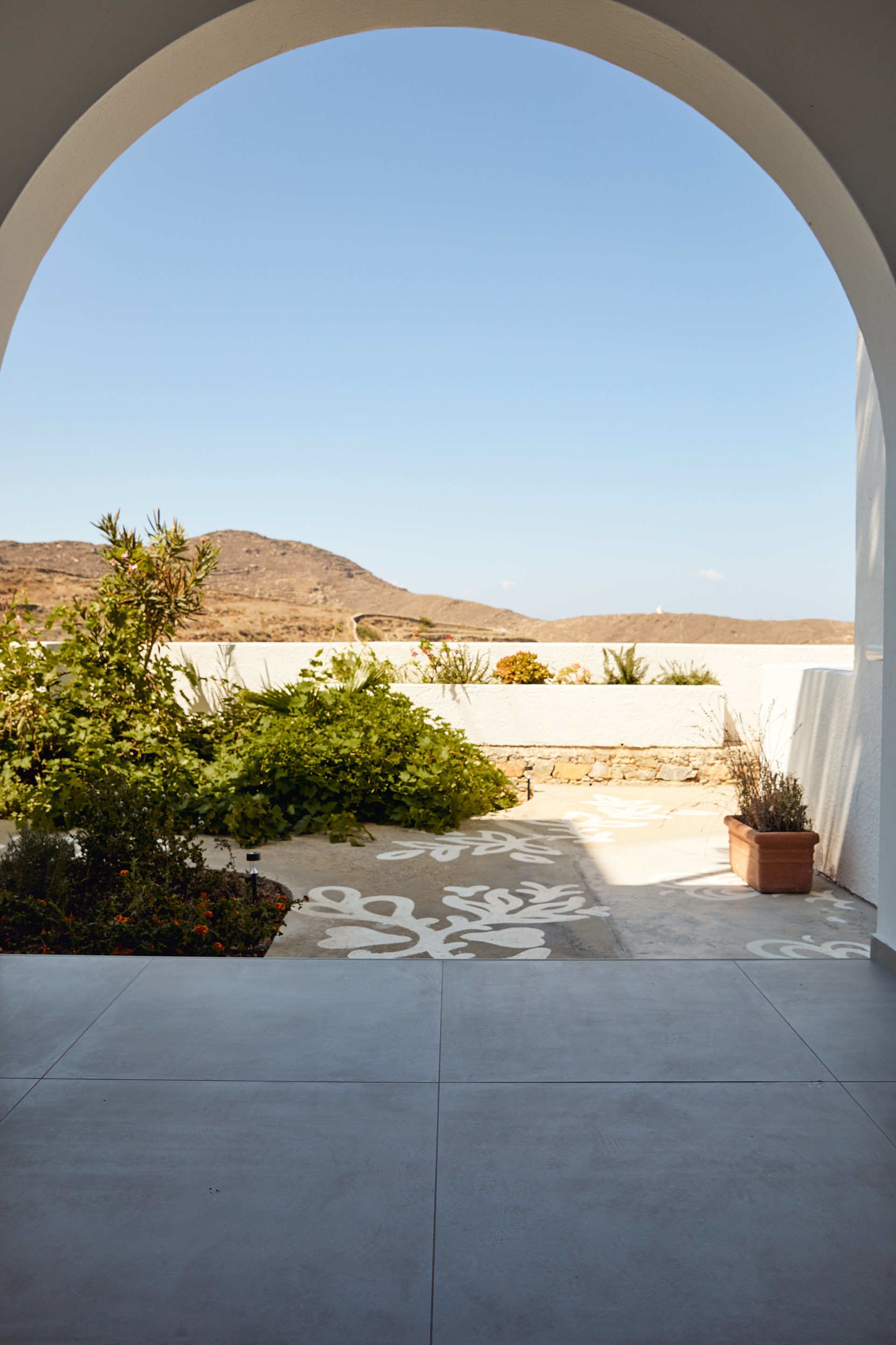 An arched doorway leading to a patio with a patterned floor, potted plants, and a view of a desert landscape.
