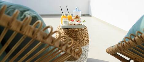 A wicker table with a tray of food and drinks on a balcony overlooking a mountainous landscape.