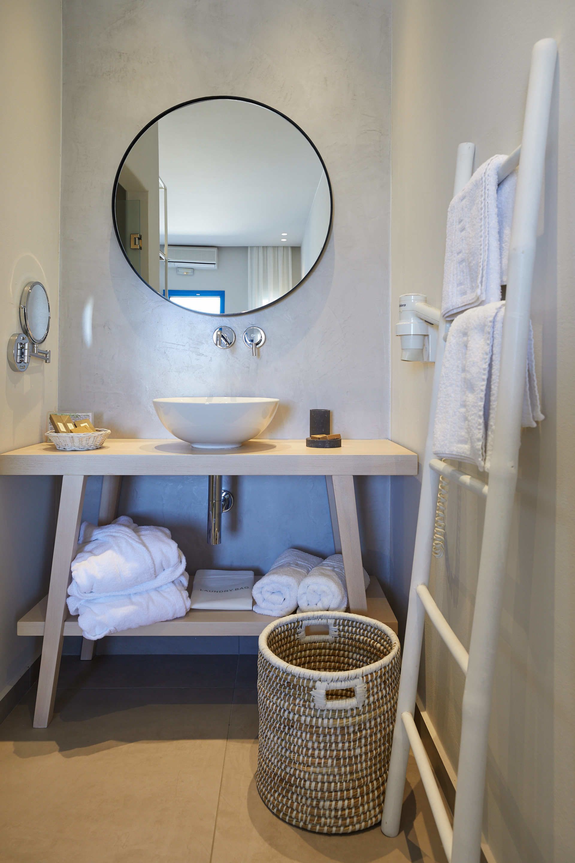Une salle de bain moderne avec un miroir rond, un lavabo blanc et un porte-serviettes.