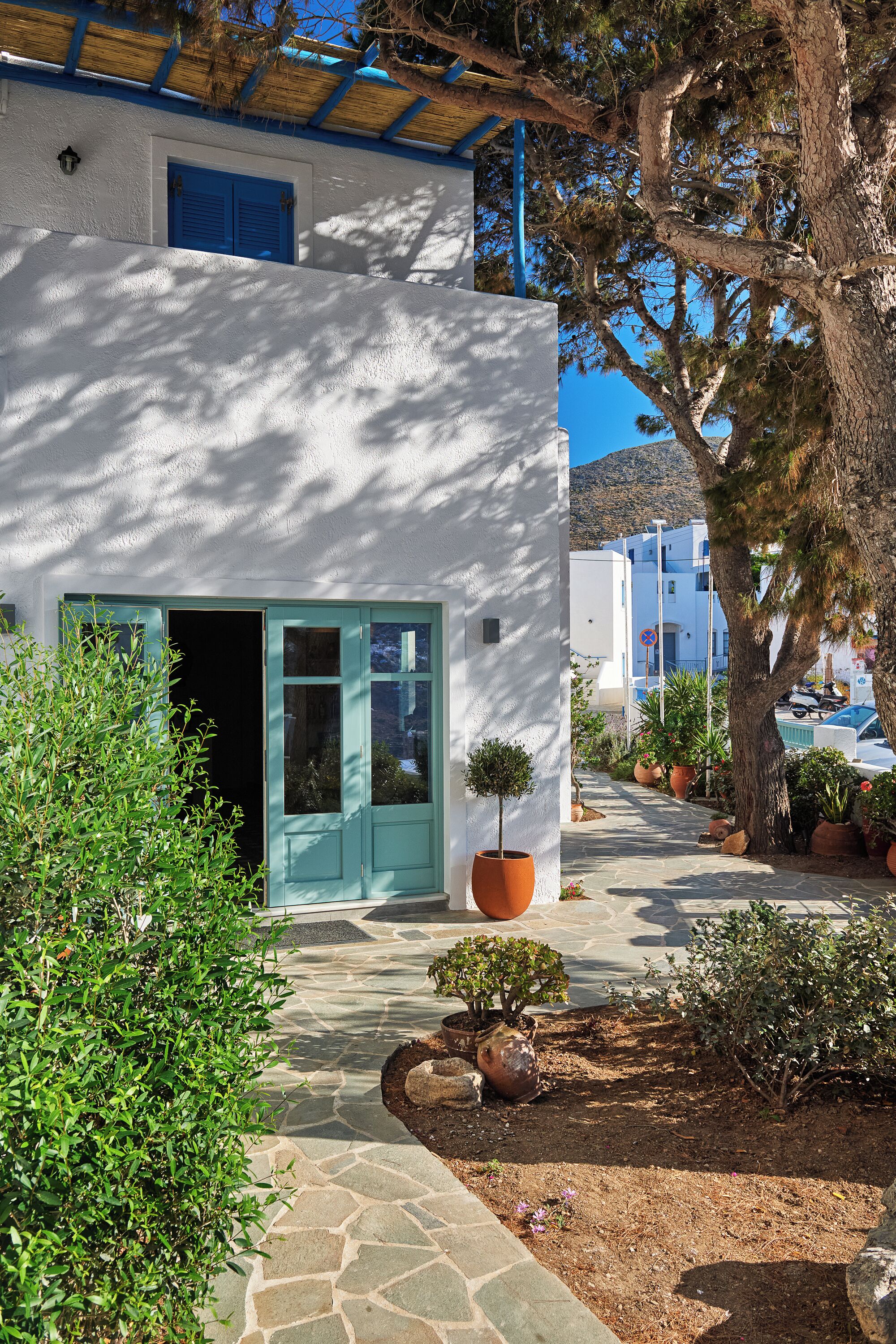 A white building with a blue door and windows, surrounded by potted plants and a stone pathway.