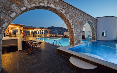 A stone archway leading to a pool area with lounge chairs and a bar.