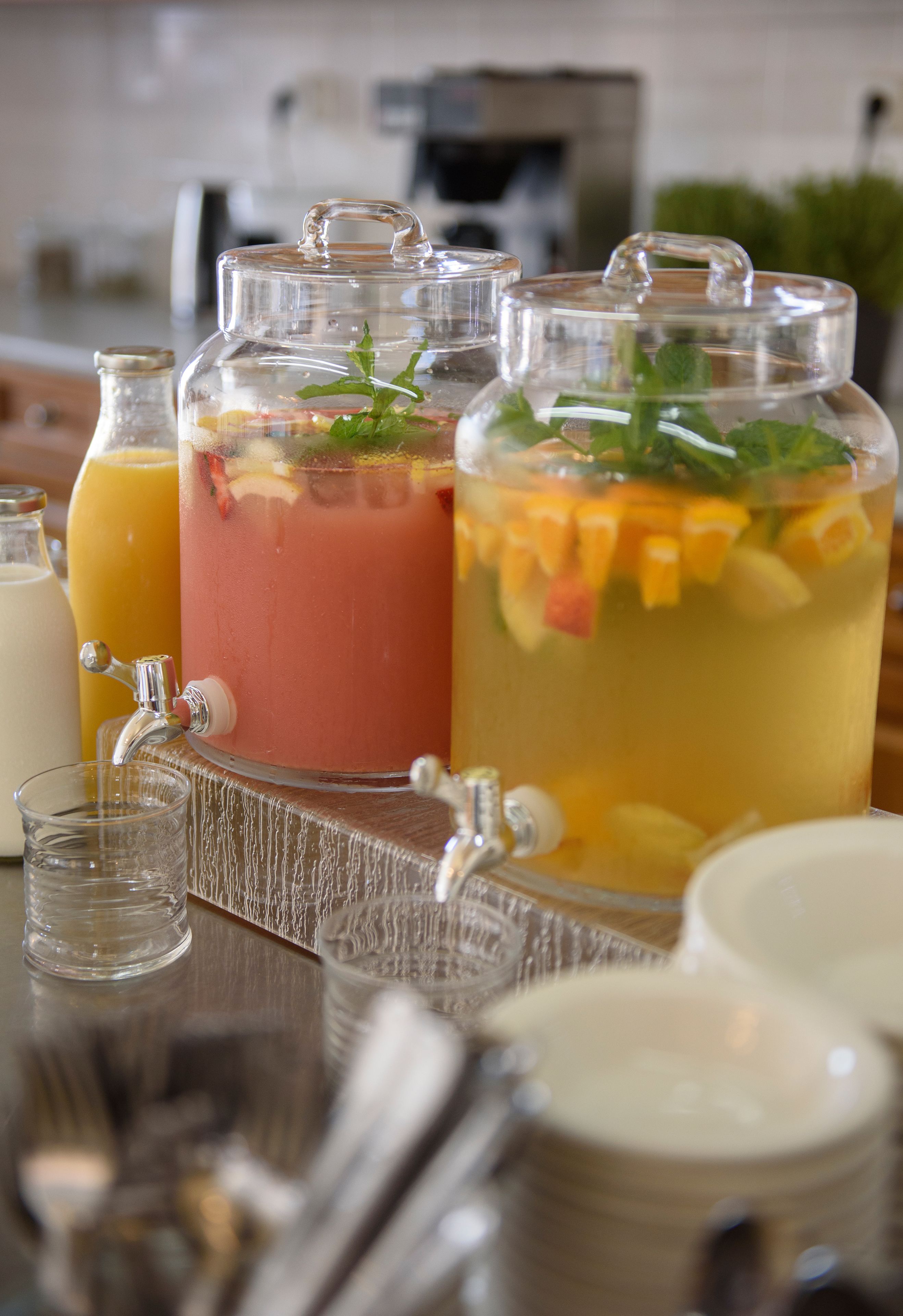 A kitchen counter with a fruit punch dispenser, a glass of orange juice, and a pitcher of water.