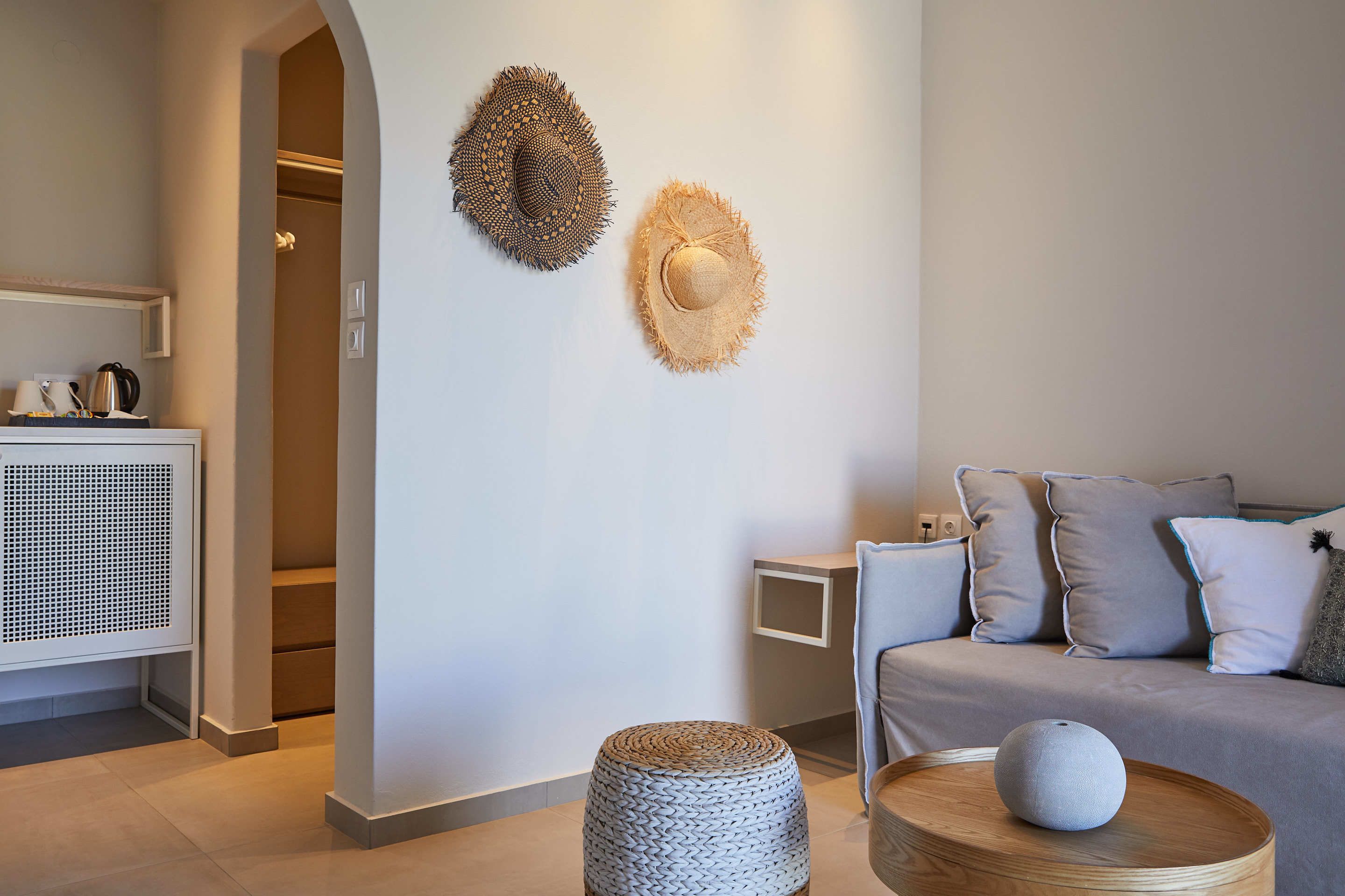 Een moderne woonkamer met een bank, twee hoeden aan de muur, een bijzettafeltje met decoratie, en een klein nachtkastje.