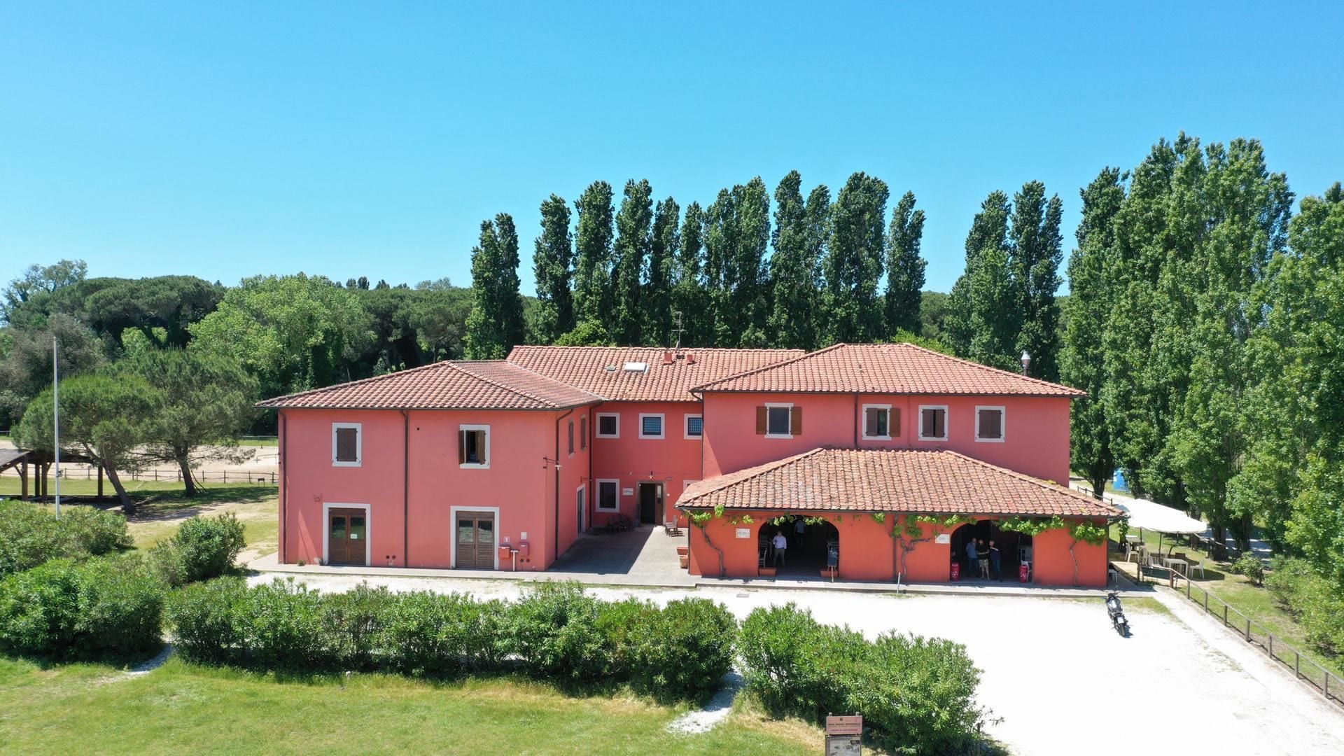 A large, two-story building with a red-tiled roof, surrounded by greenery and trees.