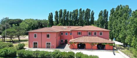 A large, two-story building with a red-tiled roof, surrounded by greenery and trees.