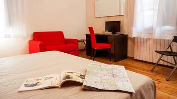 Une chambre d’hôtel avec un lit, un bureau, une chaise rouge et une carte posée sur le lit.
