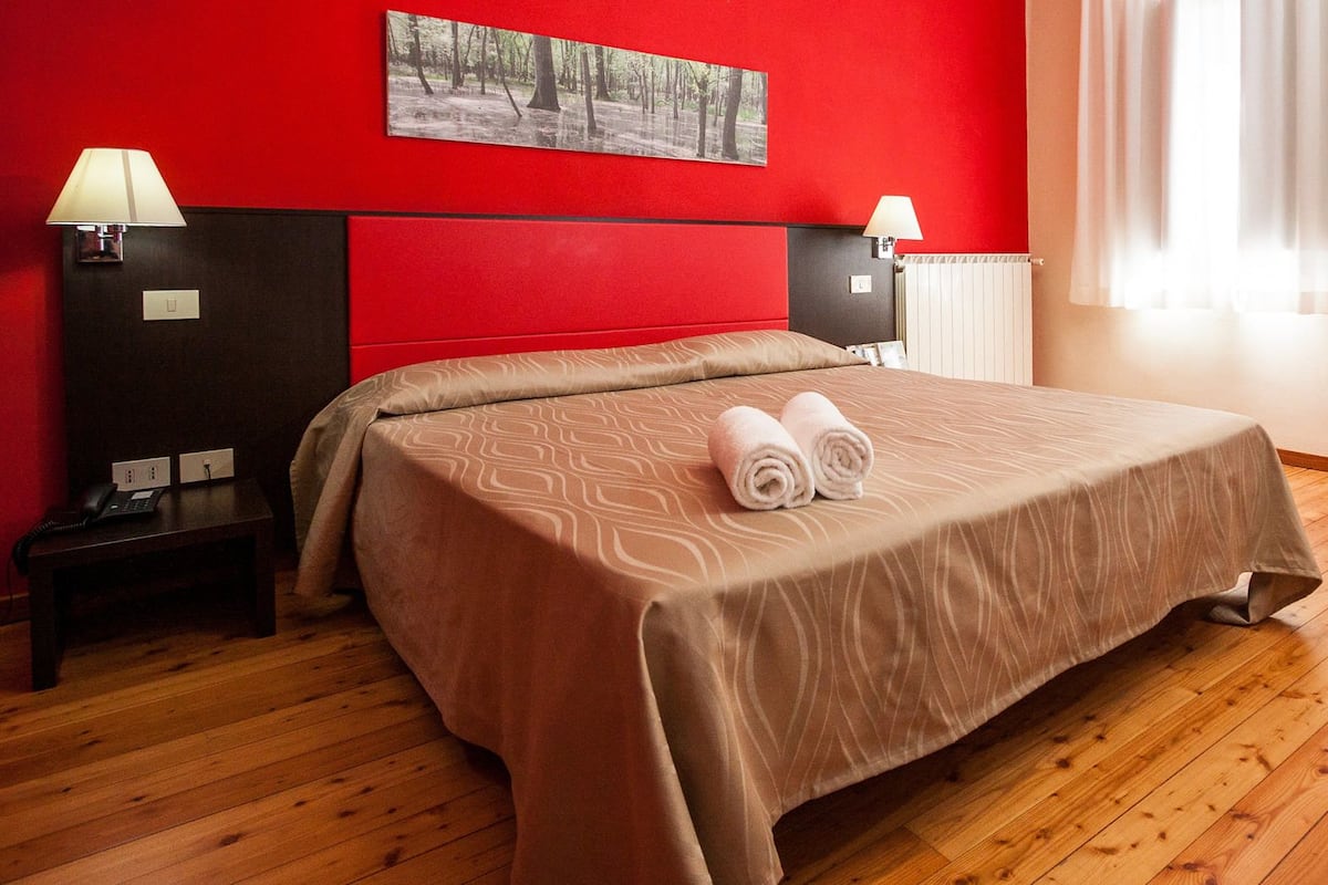 A hotel room with a large bed, two bedside tables, a red sofa, and a window with curtains.