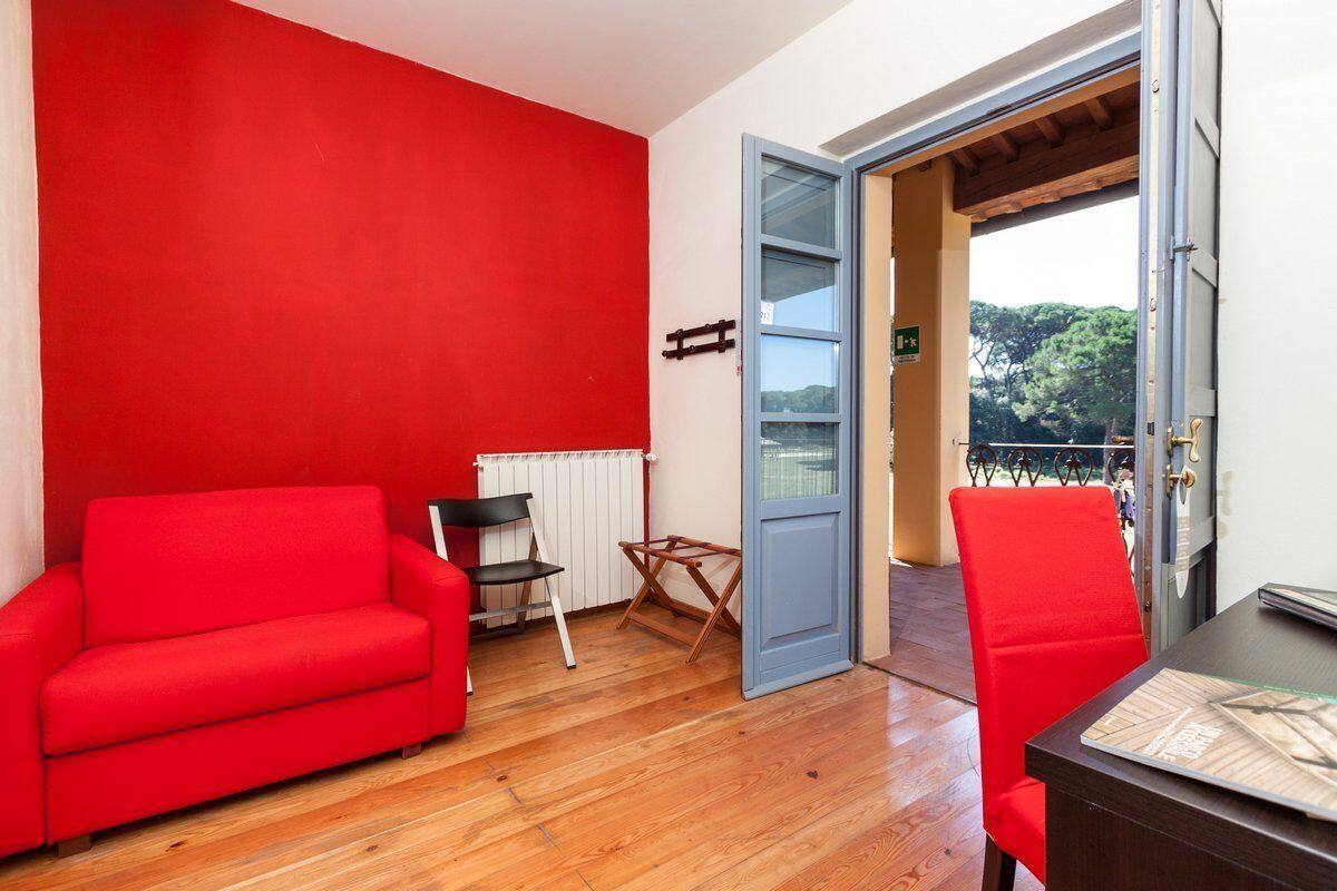 A room with a red sofa, a small table, and a chair. There is a window with a view of trees and a building.