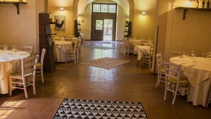 A restaurant with round tables, chairs, and a patterned rug on the floor. - Hotel Casale la Sterpaia Pisa (San Giuliano Terme)