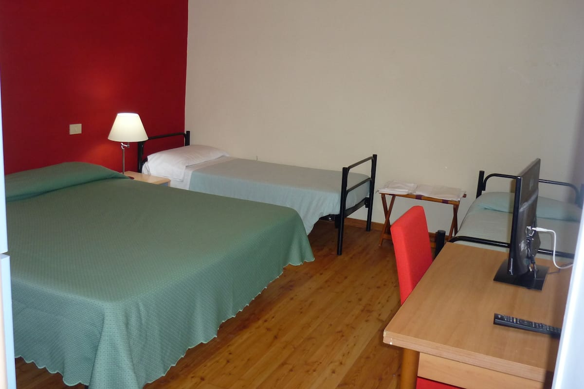 A room with two single beds, a desk with a chair, a lamp, and a television.