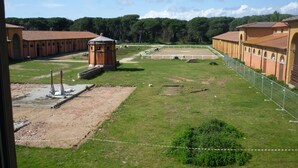 A large, open courtyard with a tennis court, surrounded by buildings with arched windows and a central tower. - Hotel Casale la Sterpaia Pisa (San Giuliano Terme)