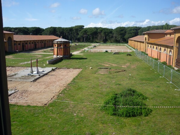 Une vaste cour ouverte, dotée d’un terrain de tennis et entourée de bâtiments aux fenêtres en arc de cercle, avec une tour centrale.