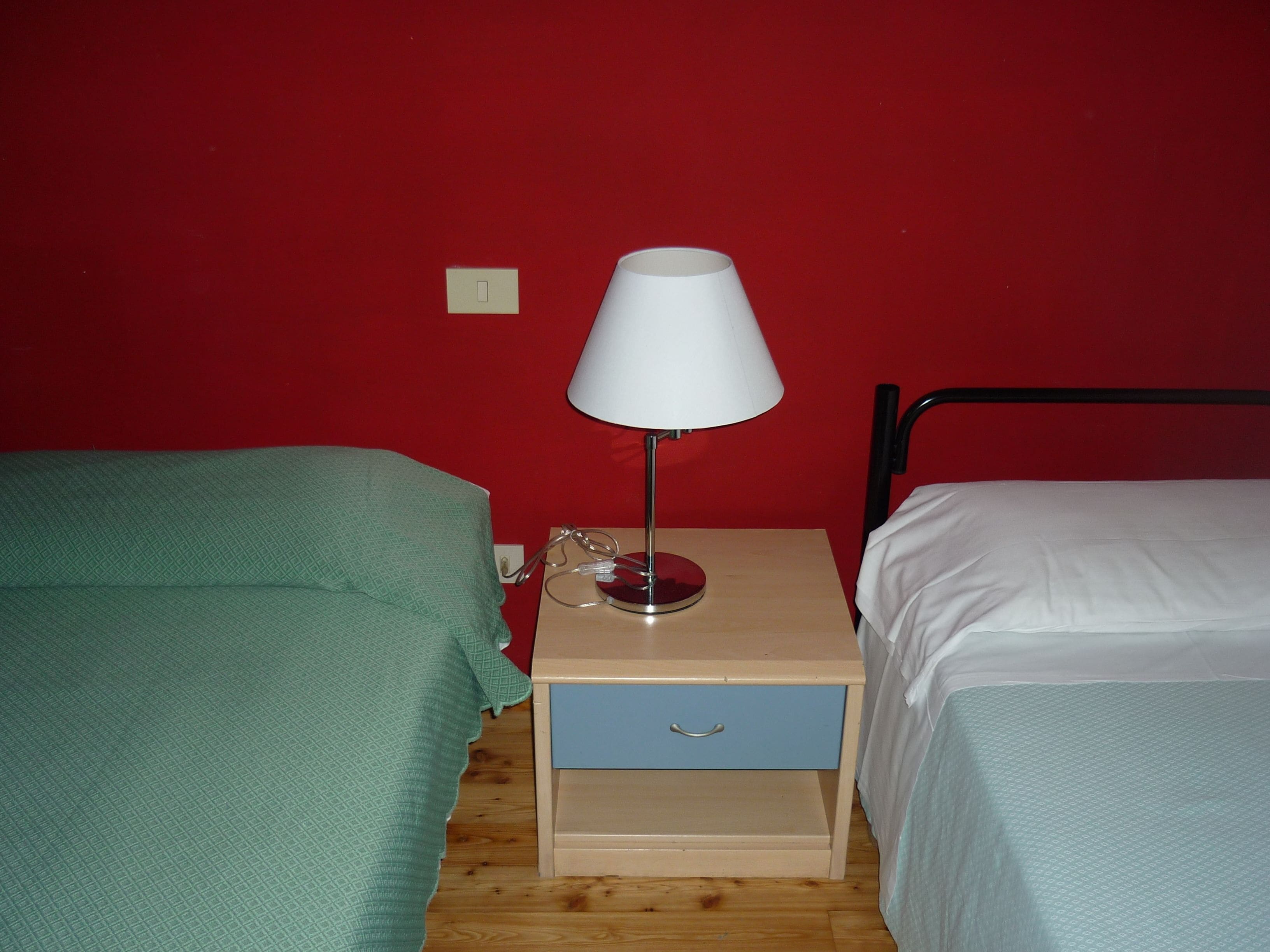 A small room with two single beds, a nightstand with a lamp, and a drawer.