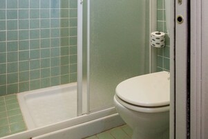 Un baño con inodoro, cabina de ducha y un rollo de papel higiénico en la pared.