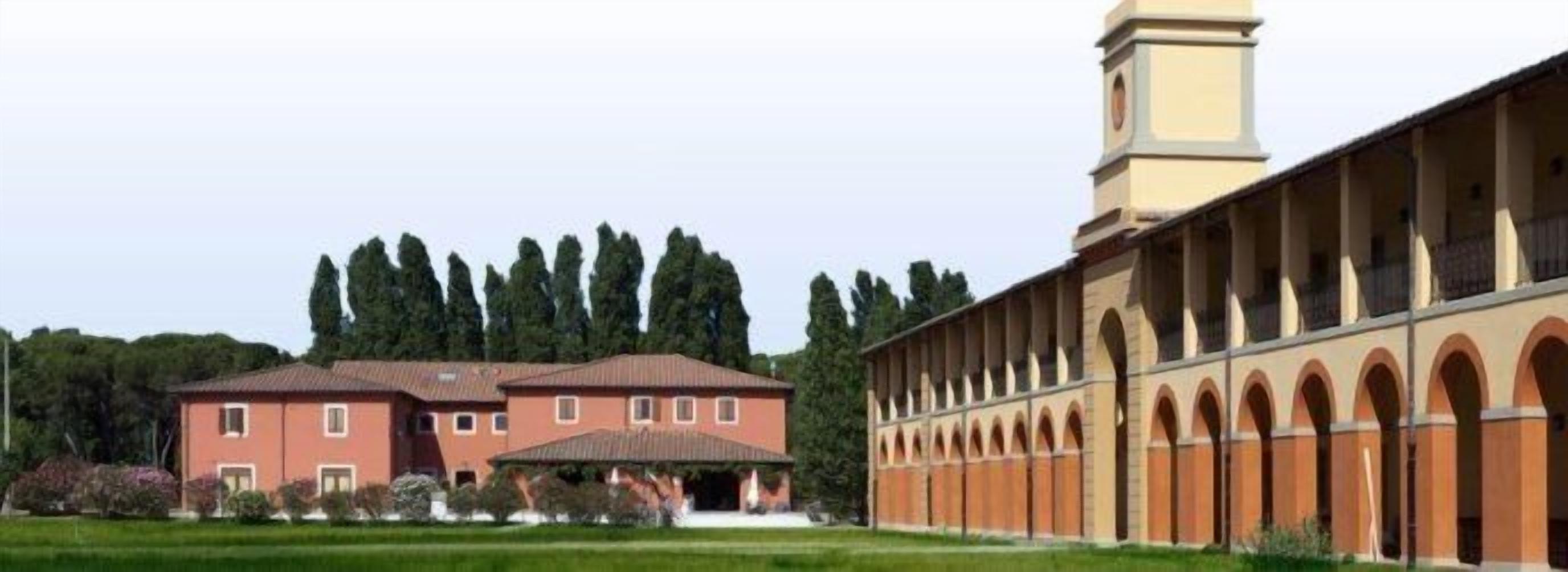 A building with a long corridor with arches, a separate building with a red facade, and a tower.