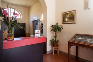 Un área de recepción con un mostrador rojo, una planta en maceta, un cuadro en la pared y una vitrina.