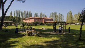 A park with a playground, benches, and a building in the background. - Hotel Casale la Sterpaia Pisa (San Giuliano Terme)