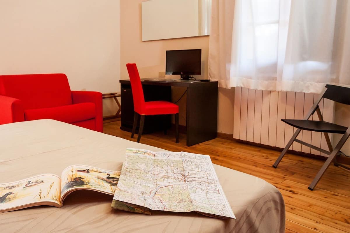A hotel room with a bed, a desk, a red chair, and a map on the bed.