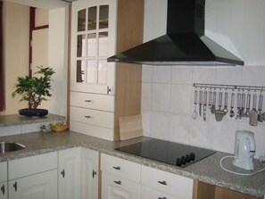 Uma cozinha com armários brancos, uma coifa preta, um balcão com cafeteira e um suporte para utensílios.