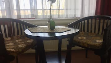 Une table ronde surmontée d’un set de table en fibres tressées, deux chaises avec des coussins à motifs et un vase vert contenant une plante.