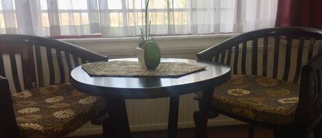 A round table with a woven placemat, two chairs with patterned cushions, and a green vase with a plant.